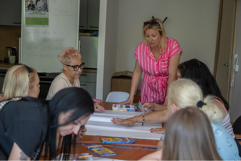Wielkopolskie Stowarzyszenie Inicjatyw Lokalnych „Zielona Kropka” Zdjęcie przedstawia grupę kobiet, które wspólnie pracują nad projektem. Jedna z nich stoi, pozostałe siedzą. Autorem fotografii jest Maciej Motylewski.