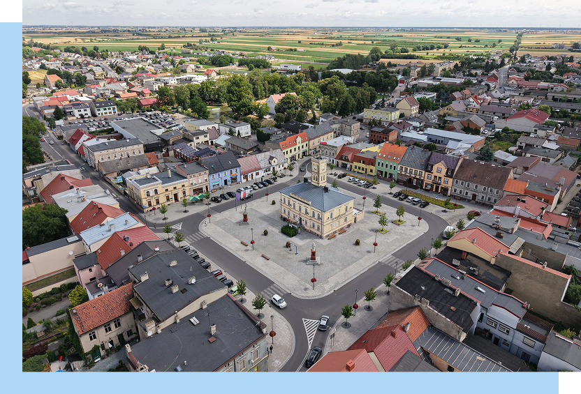 Fotografia z lotu ptaka ukazuje miejski rynek. To duży plac, otoczony niewielkimi, gęsto ustawionymi budynkami. W centralnej części placu znajduje się ratusz. Autorem zdjęcia jest Maciej Motylewski.