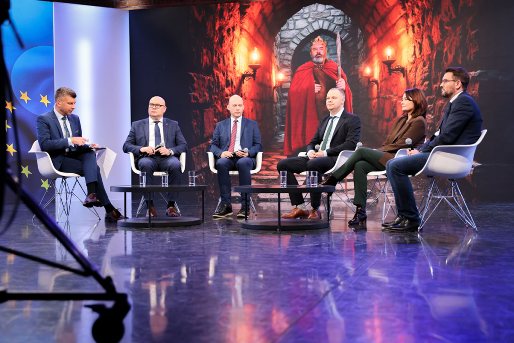 Zdjęcie przedstawia sześć osób: kobietę i pięciu mężczyzn, wszystkich elegancko ubranych, w trakcie debaty. Autorem fotografii jest Maciej Motylewski.