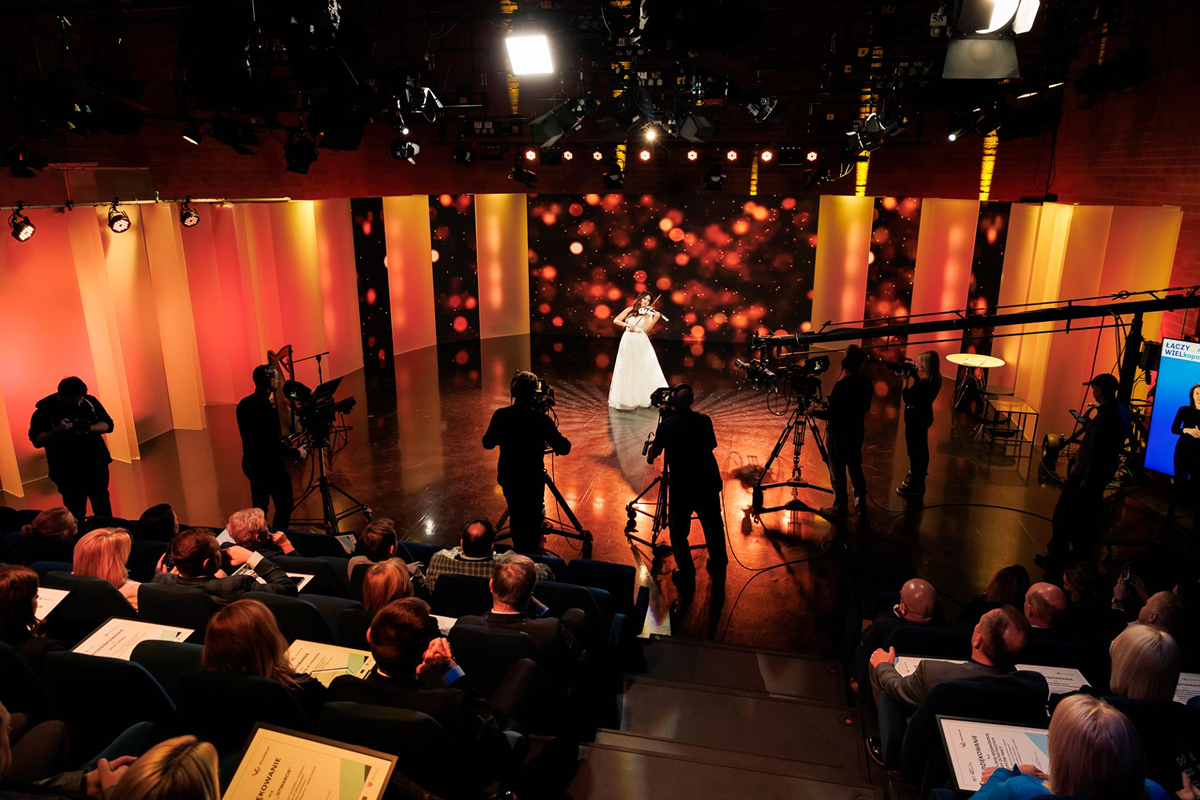 Zdjęcie wykonano w studio telewizyjnym. Widać na nim skrzypaczkę w trakcie grania utworu. Jest filmowana przez kilka kamer. Widać także licznie zgromadzoną publiczność. Fotografia pochodzi z archiwum Urzędu Marszałkowskiego Województwa Wielkopolskiego.