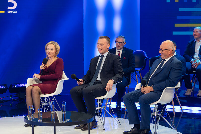 4 Na scenie siedzi dwóch elegancko ubranych mężczyzn oraz kobieta w bordowej sukience. Wszyscy mają mikrofony, gdyż uczestniczą w debacie. W tle widać kolejne osoby. Zdjęcie pochodzi z archiwum Urzędu Marszałkowskiego Województwa Wielkopolskiego.